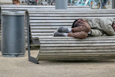 Bedürftige Person schläft auf einer Parkbank, ein Zeichen der Notwendigkeit für verbesserte Sozialhilfe.